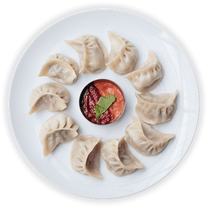 "Plate of steamed dumplings arranged in a circle around a small dish of red dipping sauce, garnished with a cilantro leaf."